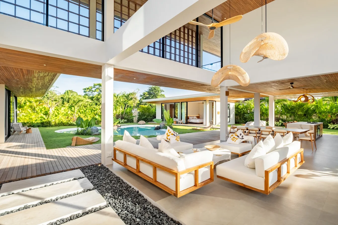 Open-air living lounge with white sofas and woven pendant lights, opening onto the pool deck