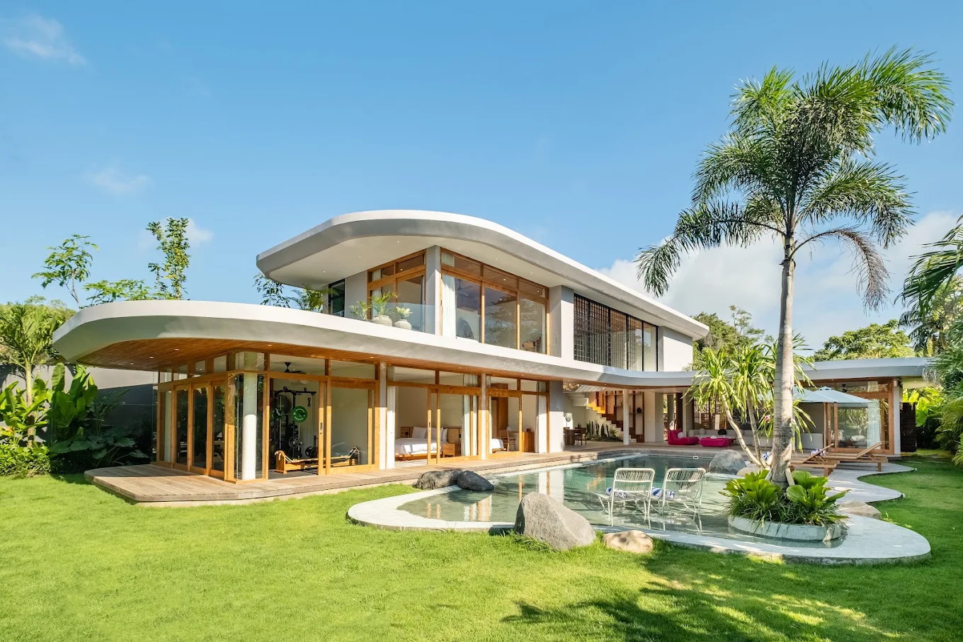 Contemporary two-story villa with curved rooflines and floor-to-ceiling glass beside an organic-form pool