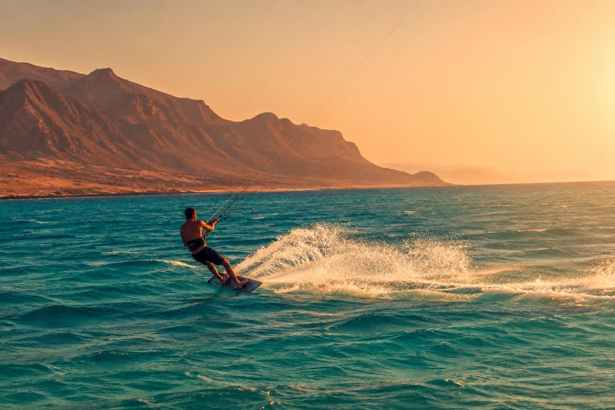 Kitesurfer carving turquoise water off a desert coastline at golden hour